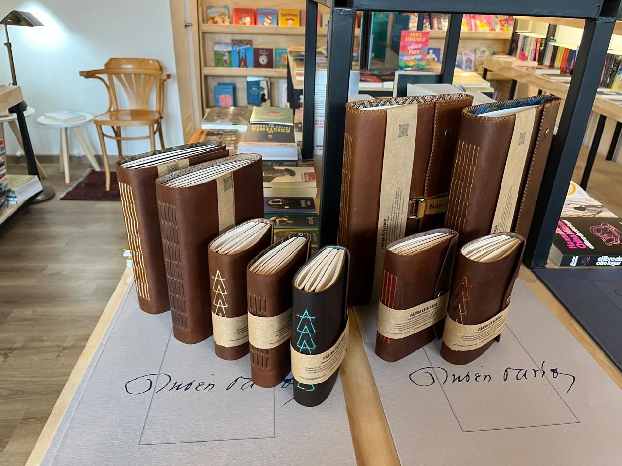 Libros encuadernados en cuero café con lomos de colores, exhibidos sobre una mesa en una librería.